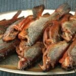 A person is holding a tray of dried fish.