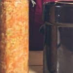 A woman is standing next to a jar of cabbage.