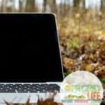 A laptop laying on the ground in the woods.