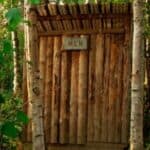 A wooden cabin in the woods with a sign that says men's restroom.