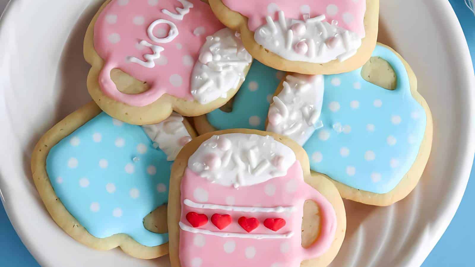 A plate of decorated cookies shaped like cups, iced in pink and blue colors with white and red details, including hearts and the word "wow.