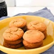 A yellow bowl holding a stack of six cookies and bars rests on a blue cloth, while a jar with a dark substance sits in the background.