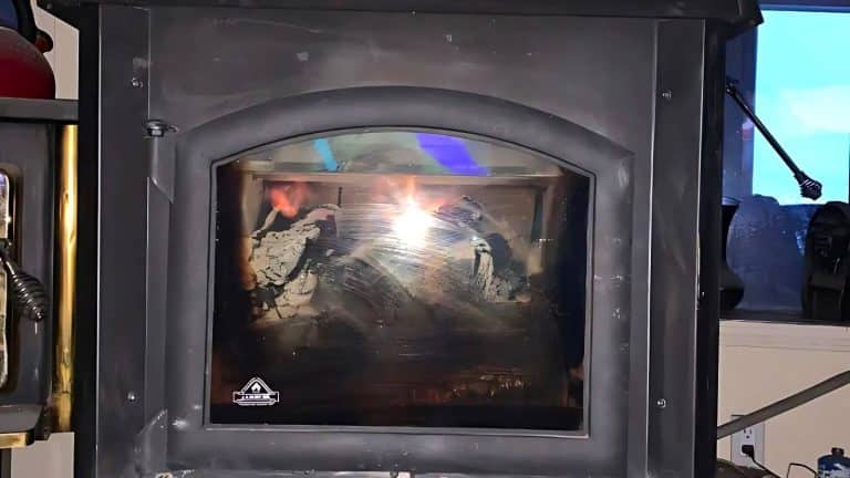 A glass-fronted wood stove with a fire burning inside. A window with a blue sky is visible to the right.