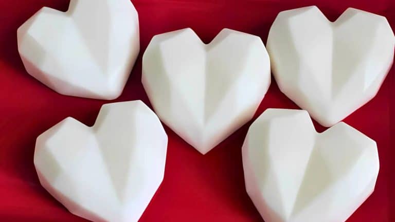 Five geometric, faceted white heart shapes arranged on a red surface.