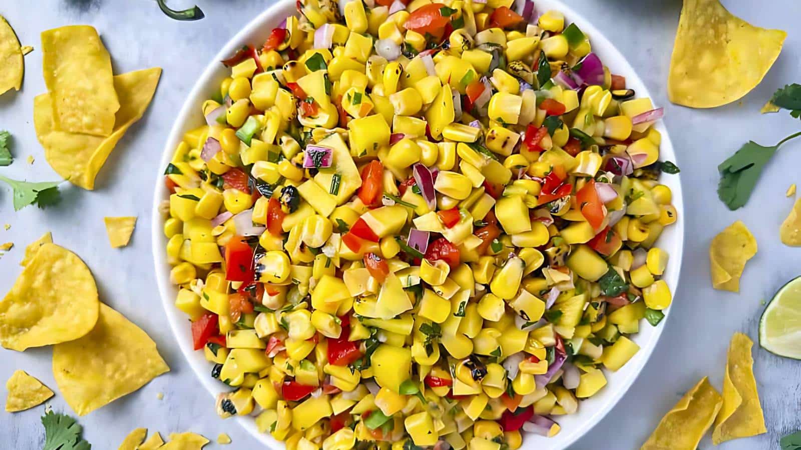 A stack of three caramel oatmeal bars is placed on a white surface, surrounded by additional bars, caramel squares, and chocolate chips. A glass of milk and a bowl of chocolate chips are in the background.