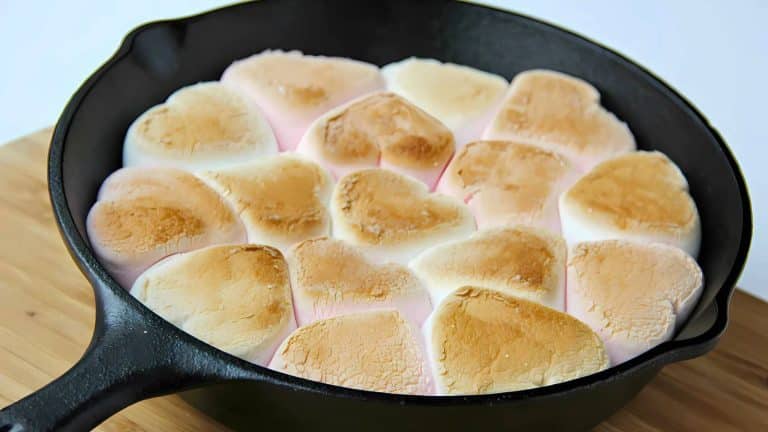 Heart-shaped marshmallows toasted in a black skillet on a wooden surface.