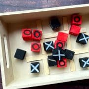 Wooden tray with small black and red blocks marked with X's and O's, arranged on a grid resembling a DIY tic-tac-toe board.