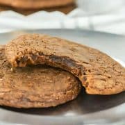 Two chocolate cookies on a silver plate, one with a bite taken out.