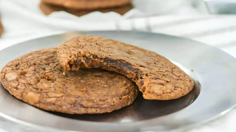 Two chocolate cookies on a silver plate, one with a bite taken out.