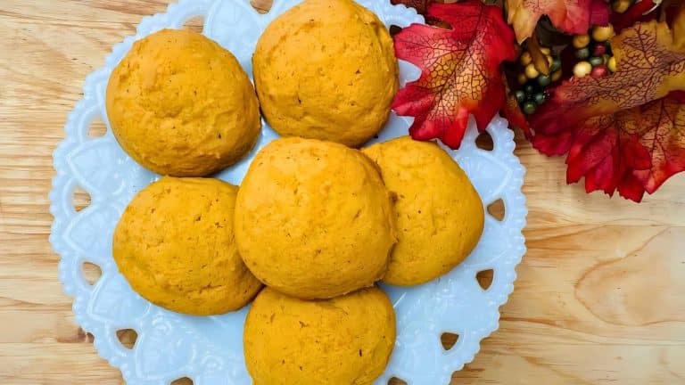 Six round brown bread rolls on a decorative white plate with red fall leaves and small berries on the side.