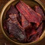 Beef jerky in a bowl on a wooden table.