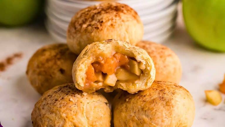 Pile of baked apple hand pies stacked on a surface. One pie is cut open, revealing a filling of cooked apples.