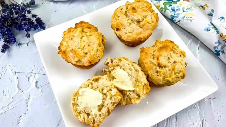 Four savory muffins on a square white plate, with one muffin cut open and topped with butter.