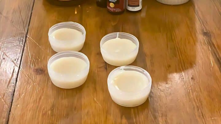 Four small plastic containers filled with a white creamy substance placed on a wooden table.