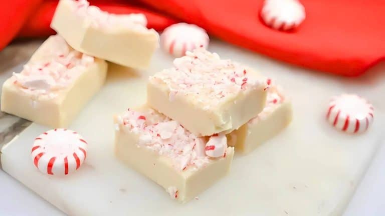 White chocolate peppermint fudge with crushed candy pieces on top, surrounded by whole peppermint candies and red fabric in the background.
