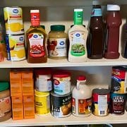 A pantry shelf stocked with various food items and condiments, including jars, bottles, and boxes of packaged goods.