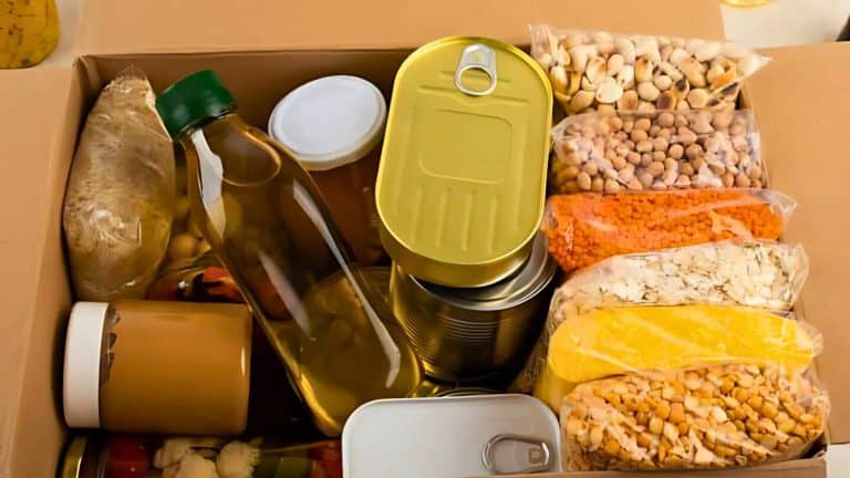 A cardboard box filled with various non-perishable food items, including canned goods, a bottle of oil, and packages of grains and legumes.