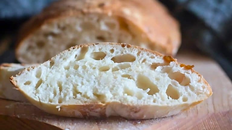 Close-up of sliced bread with a crusty exterior and soft, airy interior, on a wooden cutting board.