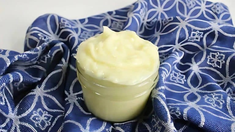 A small glass jar filled with creamy white mayonnaise, a great example of simple sustainable swaps, sits on a blue patterned cloth.
