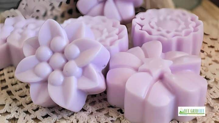 Purple flower-shaped soaps on a lace surface with a logo in the bottom right corner.