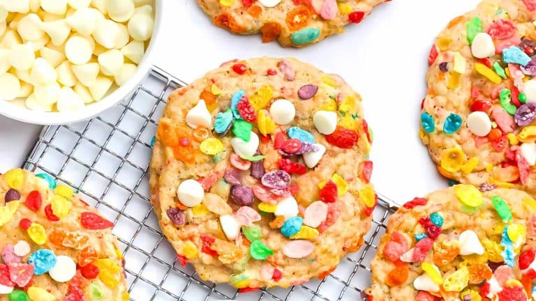 Cookies topped with colorful cereal pieces and white chocolate chips rest on a cooling rack next to a bowl of white chocolate chips.