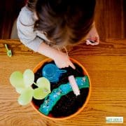 a child doing a craft on a small planter with bright blue paint and soil