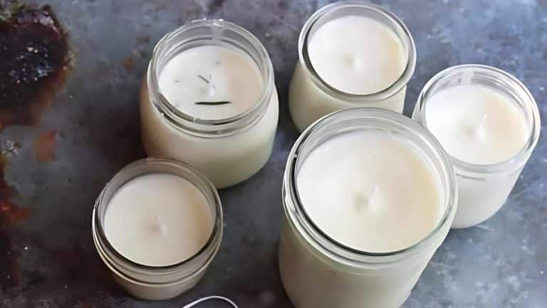 Five white candles in glass jars arranged on a textured gray surface.