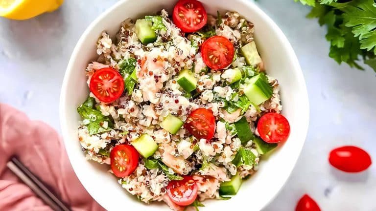A bowl of quinoa salad with shrimp, sliced cherry tomatoes, cucumber cubes, and fresh greens.