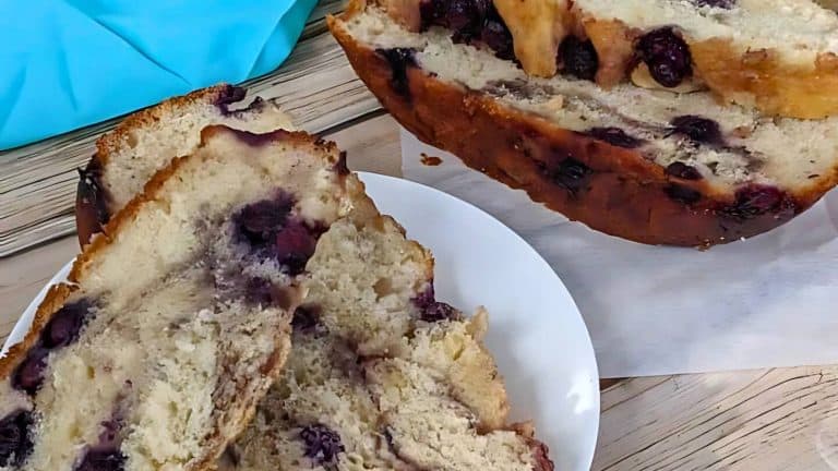 Slices of blueberry bread on a wooden table, with a portion served on a white plate.
