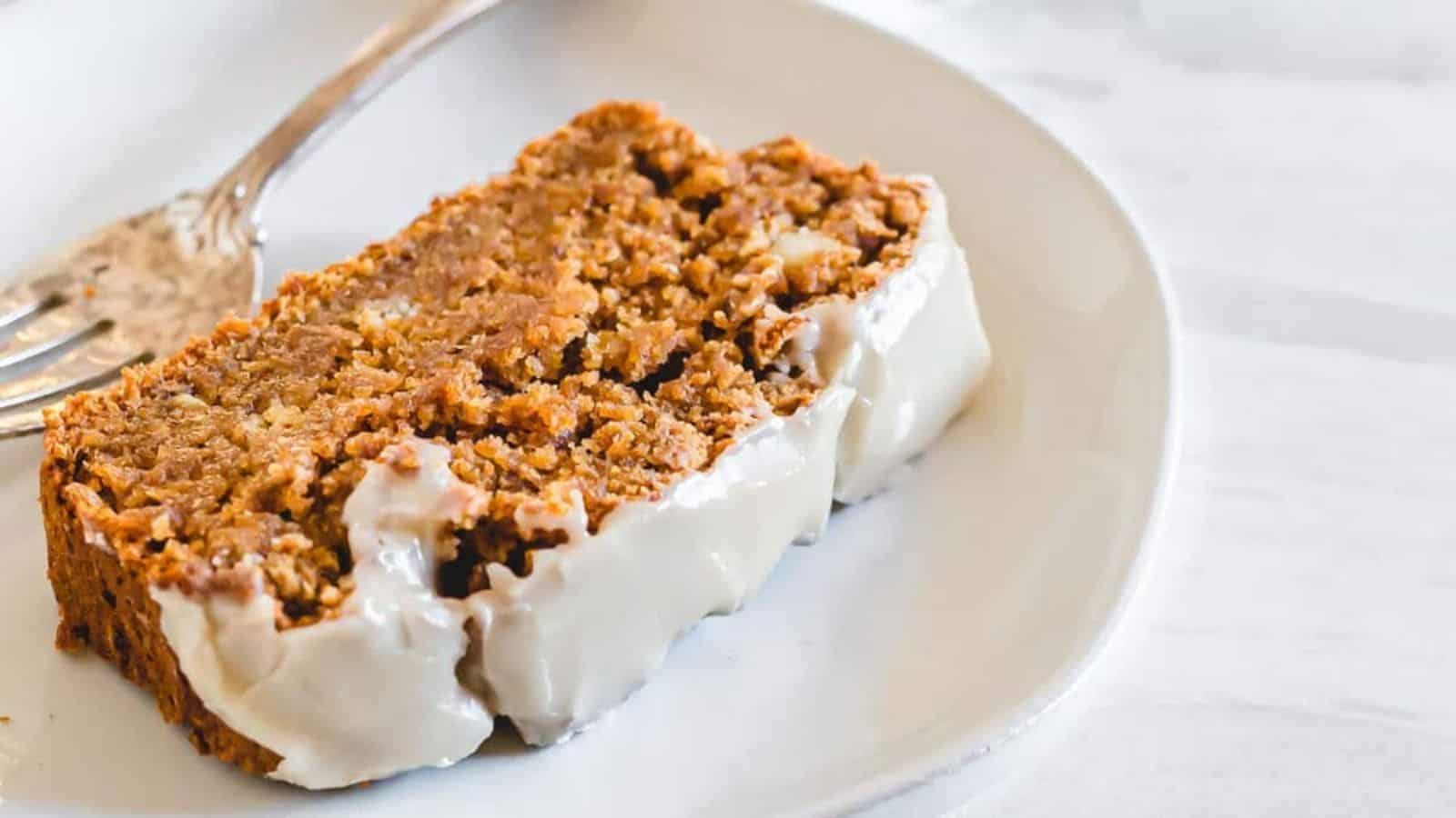 A slice of glazed banana bread on a white plate with a fork.