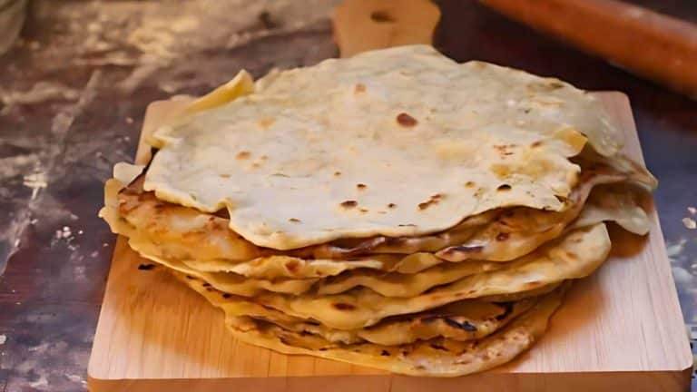 A stack of flatbreads on a wooden cutting board, with a rolling pin in the background.