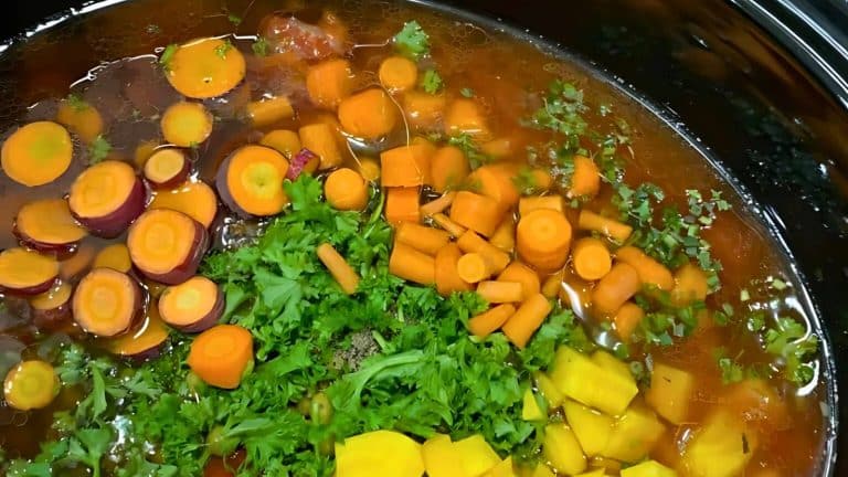 A pot filled with sliced carrots, diced yellow vegetables, and chopped parsley in a broth.