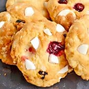Cookies with white chocolate chunks and cranberries on a dark plate.
