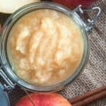 Apple butter in a jar with cinnamon and apples.