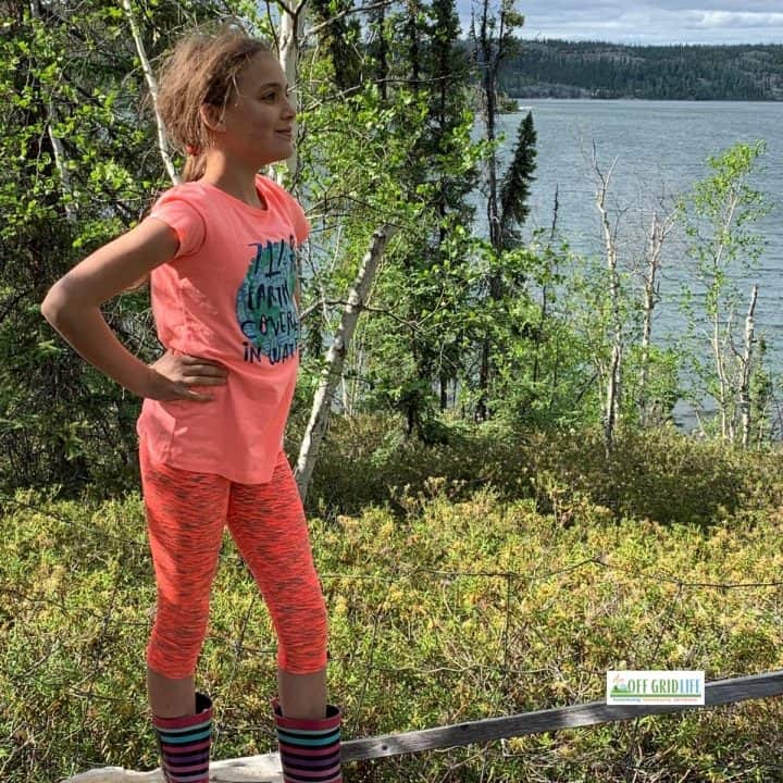 Young girl standing outside in the summer with a forest and lake in background