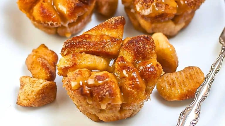 Close-up of caramel-glazed pull-apart monkey bread muffins with cinnamon coating, arranged on a white plate alongside a few scattered pieces and a fork.