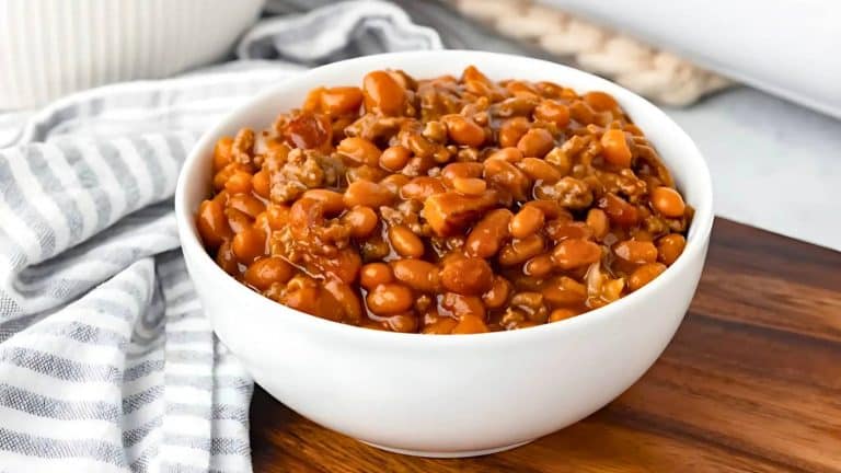 A white bowl filled with baked beans placed on a wooden surface, next to a striped cloth.