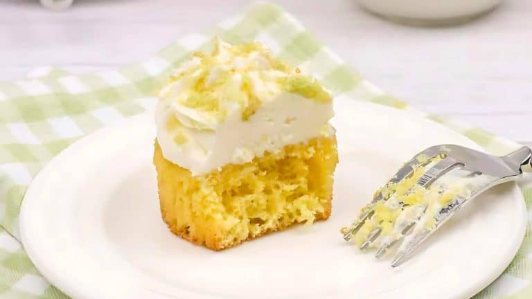 A partially eaten slice of frosted cake sits on a white plate with a fork to the side, covered with some crumbs and frosting. The background features a checkered green and white tablecloth.