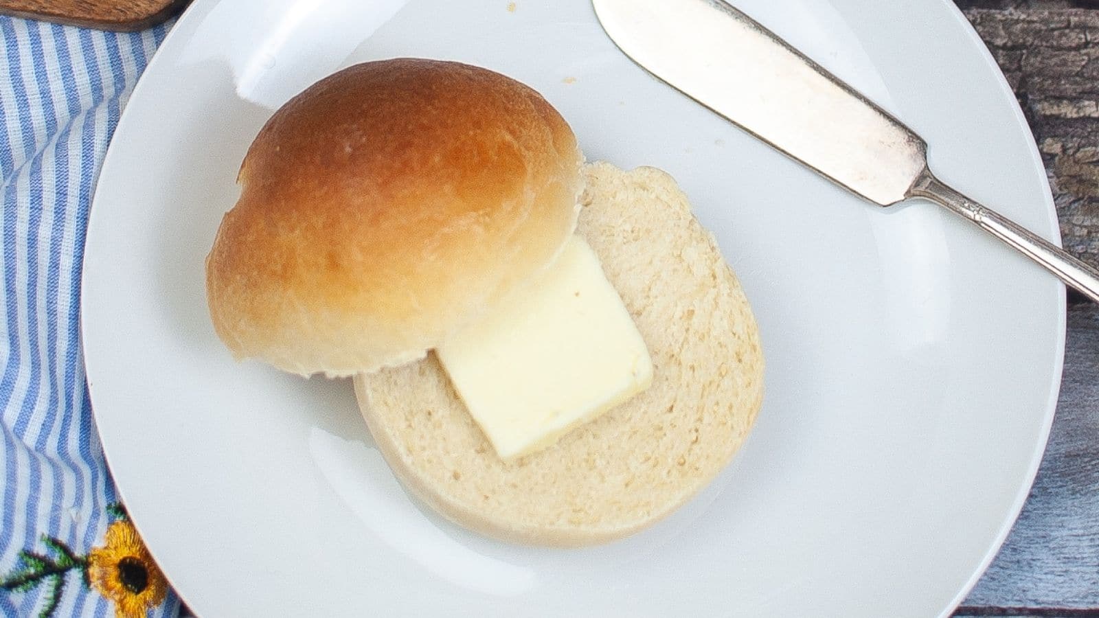 Hamburger buns on.a plate with a pat of butter on each.