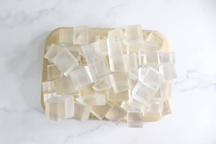 Clear rectangular gelatin cubes are arranged on a light wooden board placed on a white marble surface.