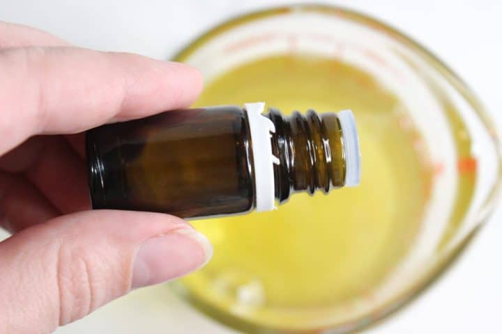 A hand holds a small amber glass bottle over a measuring cup filled with yellow liquid.