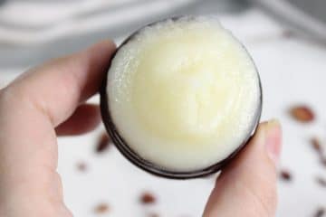 A hand holding an open container of solid, white beef tallow face cream balm.