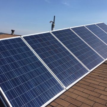 Four solar panels installed on a sloped shingle rooftop of a family living off the grid under a clear blue sky.
