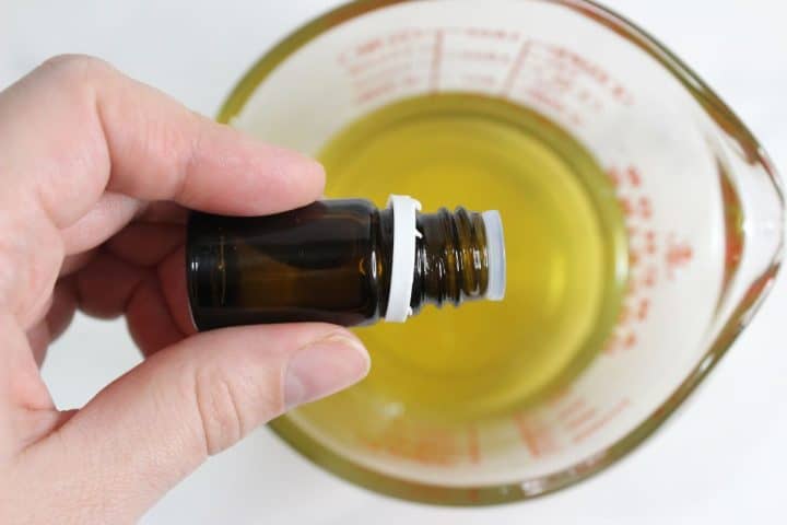 A hand holds a small brown bottle above a glass measuring cup filled with yellow liquid.