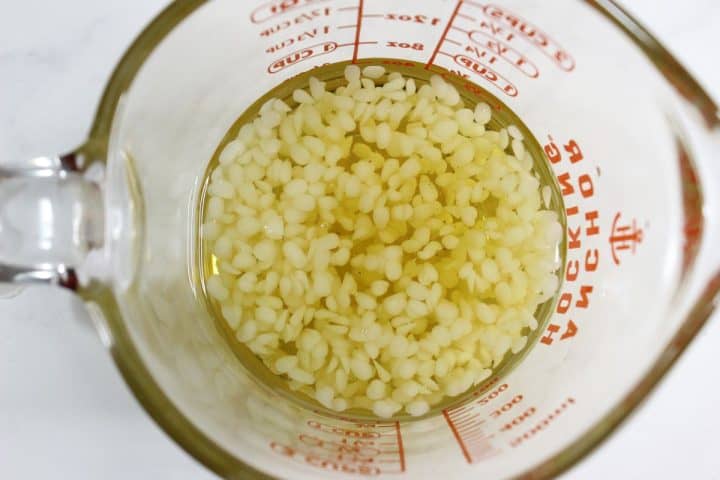 Clear glass measuring cup filled with yellowish liquid and small white pellets, viewed from above.