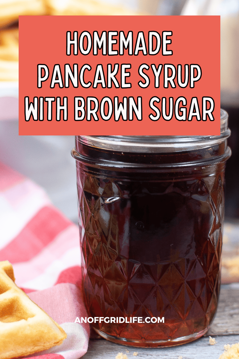 A jar of homemade pancake syrup with brown sugar on a table next to a red plaid cloth and waffle pieces.