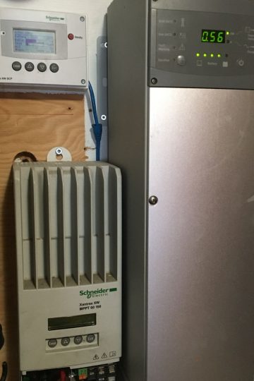 Electrical equipment, including a Schneider inverter and a display panel showing numbers, mounted on a wall with visible wiring connected to the devices for a solar stress test for off grid living.