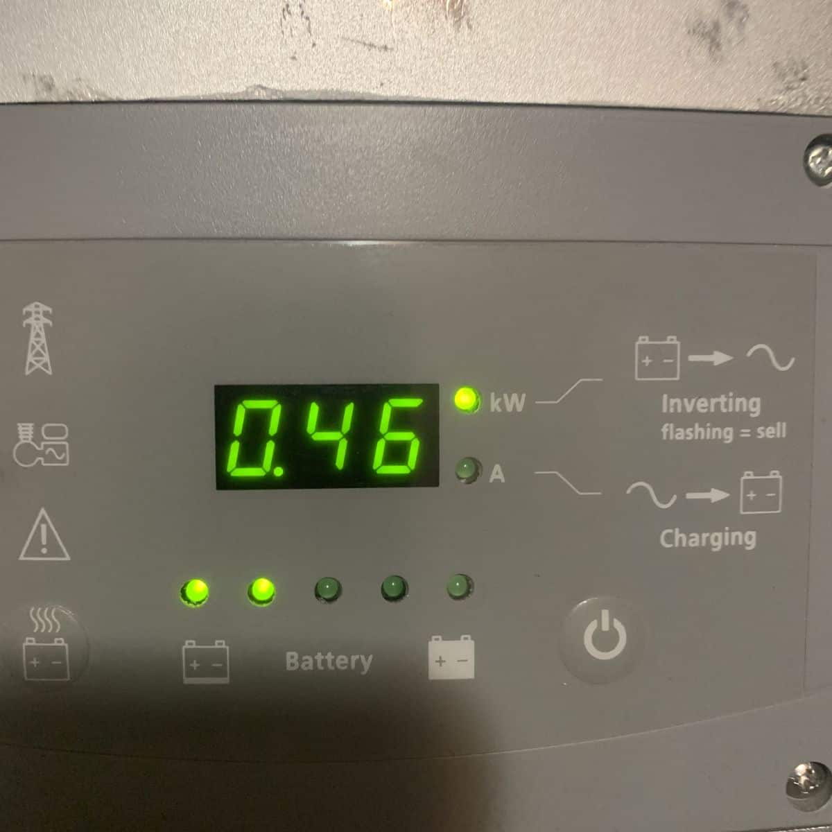 Digital display shows 0.46 kW with indicator lights on a battery inverter panel; charging and battery status icons are visible.