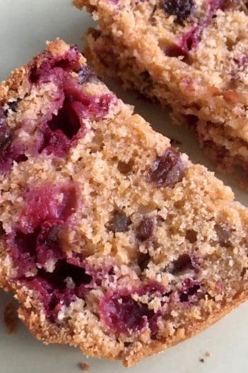 Two slices of cranberry orange loaf with visible cranberry pieces and a golden brown crumb are placed on a light-colored plate.