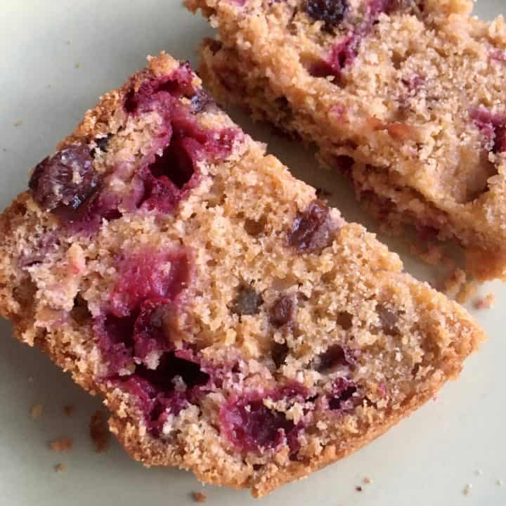 Two slices of cranberry orange loaf with visible cranberry pieces and a golden brown crumb are placed on a light-colored plate.
